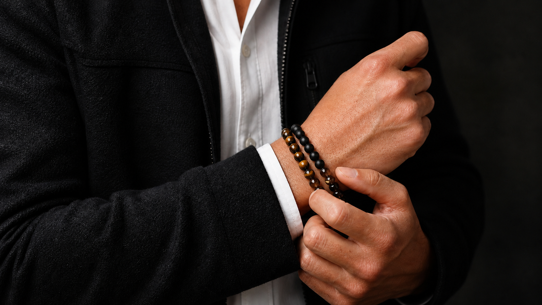 Man adjusting three tiger eye, black onyx, and smoky quartz crystal bracelets with a black jacket and white shirt
