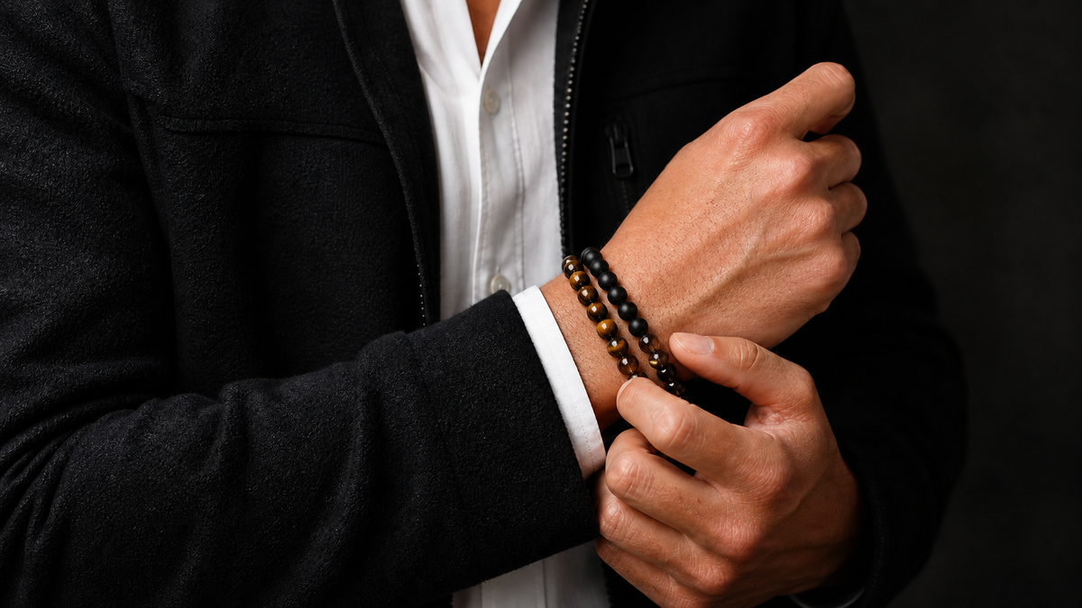 Man adjusting three tiger eye, black onyx, and smoky quartz crystal bracelets with a black jacket and white shirt