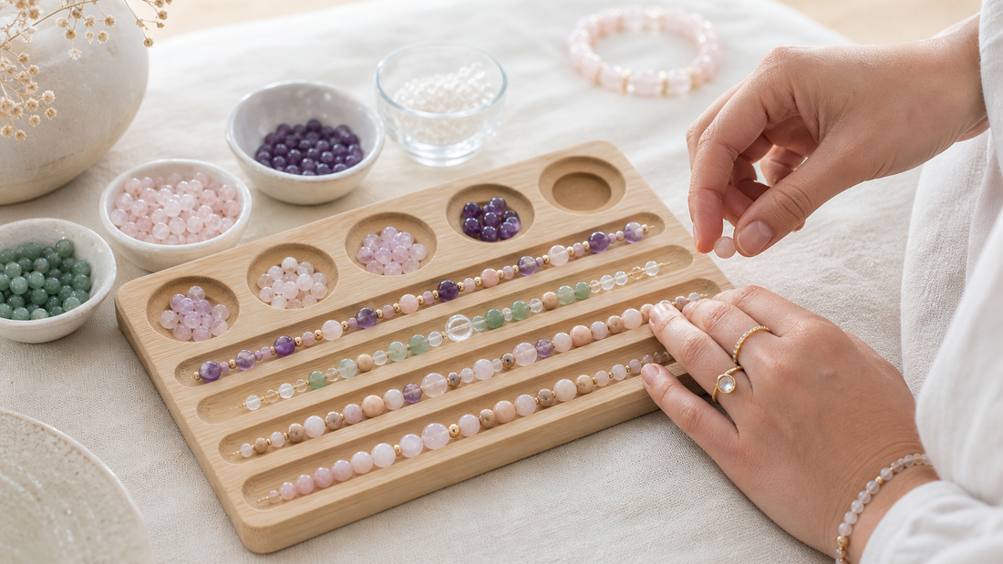 Hands arranging amethyst, rose quartz, clear quartz, and green aventurine bead patterns on a wooden bracelet design board