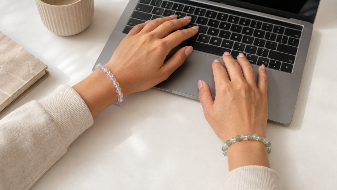 Two hands wearing natural crystal bracelets while typing on a laptop to compare left and right wrist placement