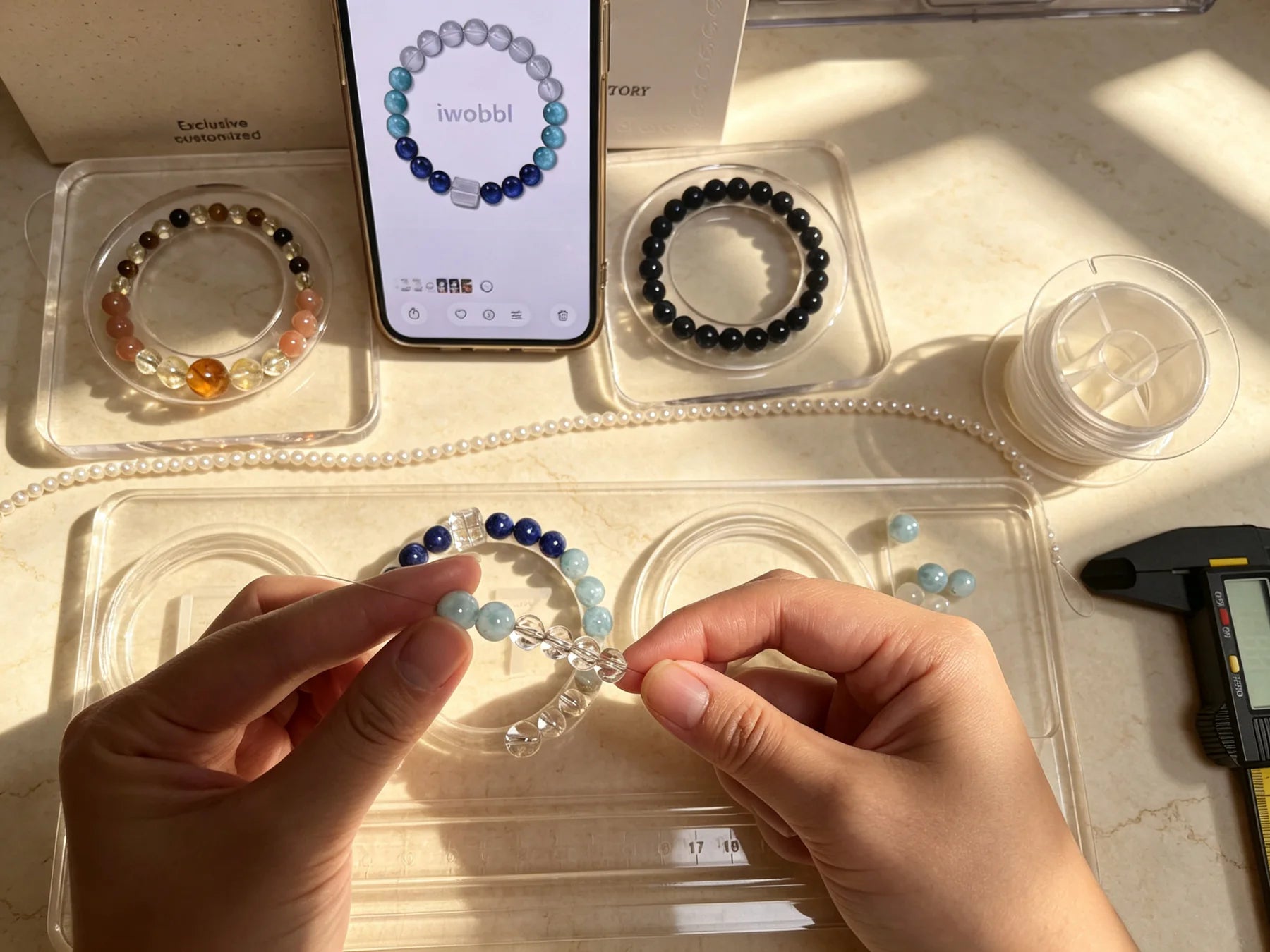 Hands assembling a crystal bracelet beside the iwobbl designer